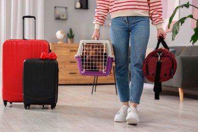 Photo of Travel with pet. Woman holding carrier with dog and bag at home, closeup