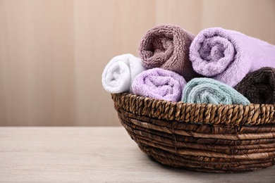 Photo of Rolled soft towels in wicker basket on wooden table. Space for text