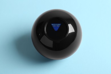 Photo of Magic eight ball with prediction Indications Say Yes on light blue background, above view