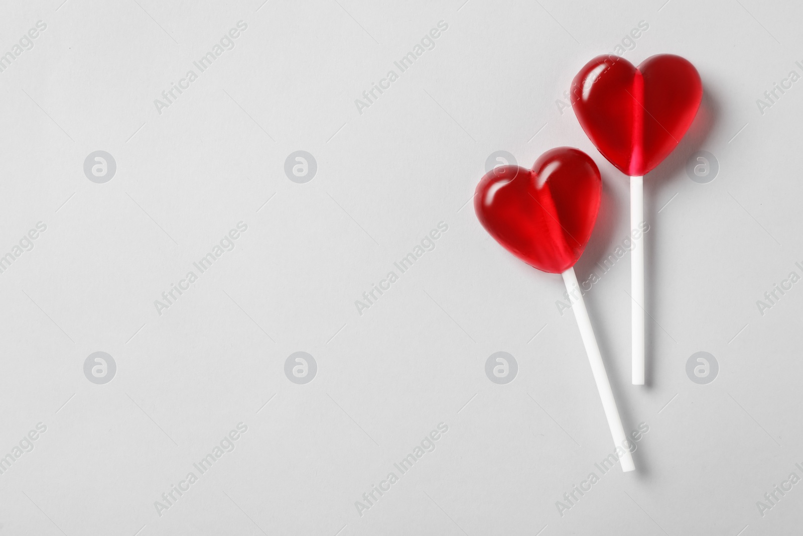 Photo of Sweet heart shaped lollipops on light grey background, flat lay with space for text. Valentine's day celebration