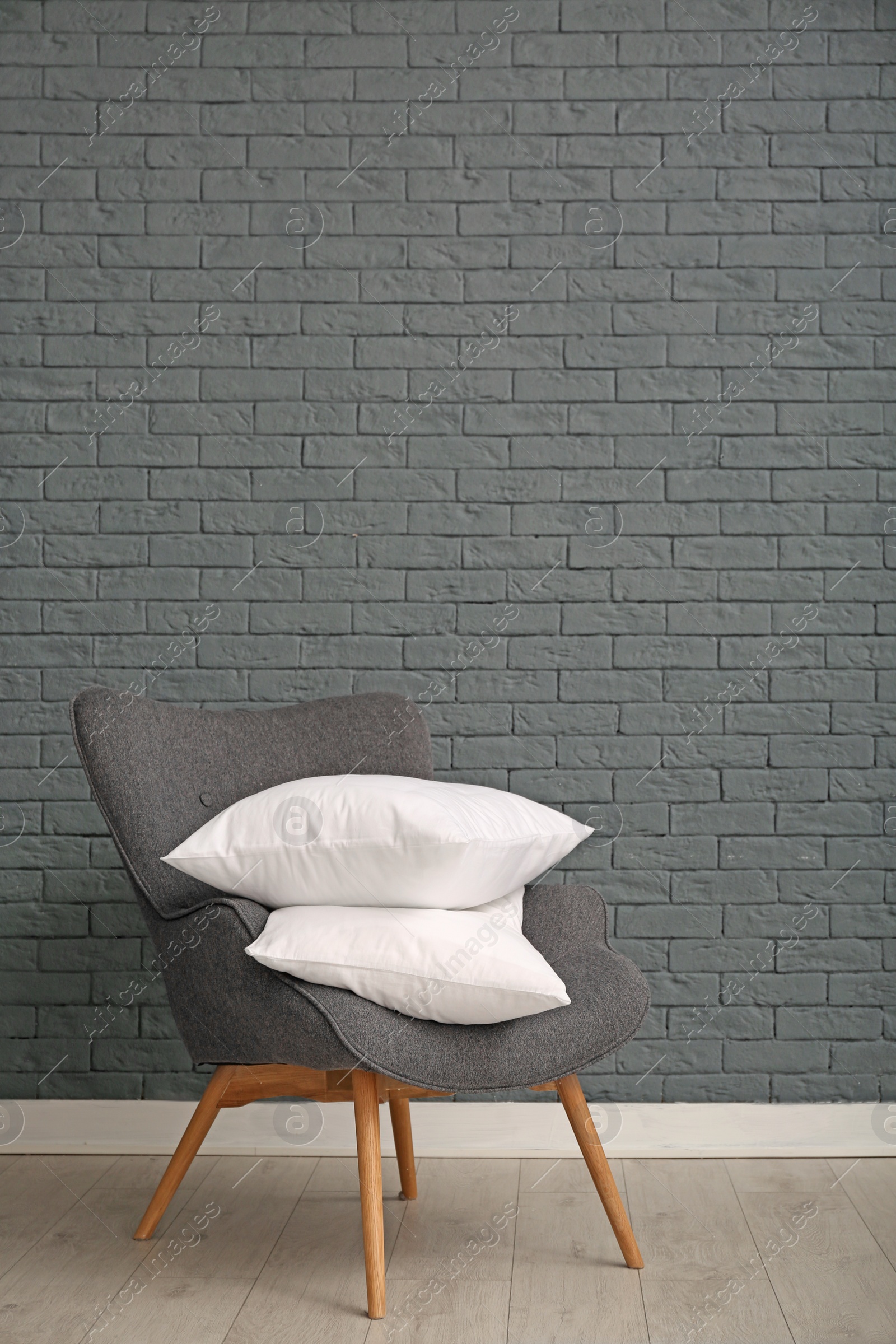 Photo of Pile of soft bed pillows on armchair near brick wall with space for text