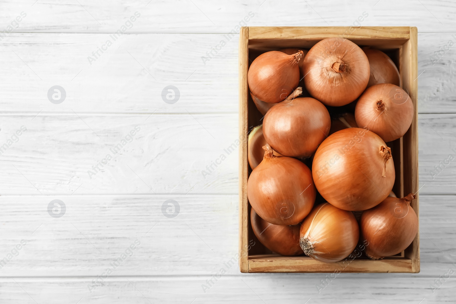 Photo of Ripe yellow onion bulbs in crate on white wooden table, top view. Space for text