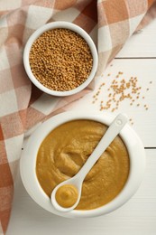 Photo of Tasty mustard sauce and dry seeds on white wooden table, flat lay