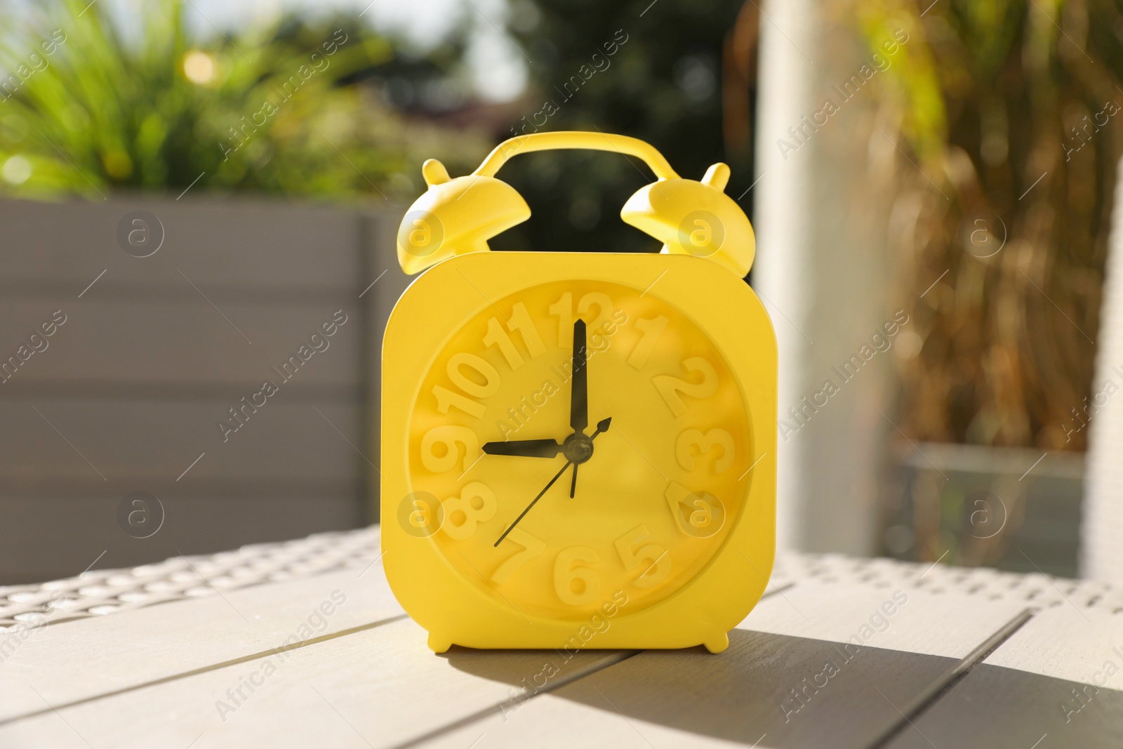 Photo of Yellow alarm clock on white wooden table outdoors at sunny morning