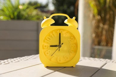 Yellow alarm clock on white wooden table outdoors at sunny morning