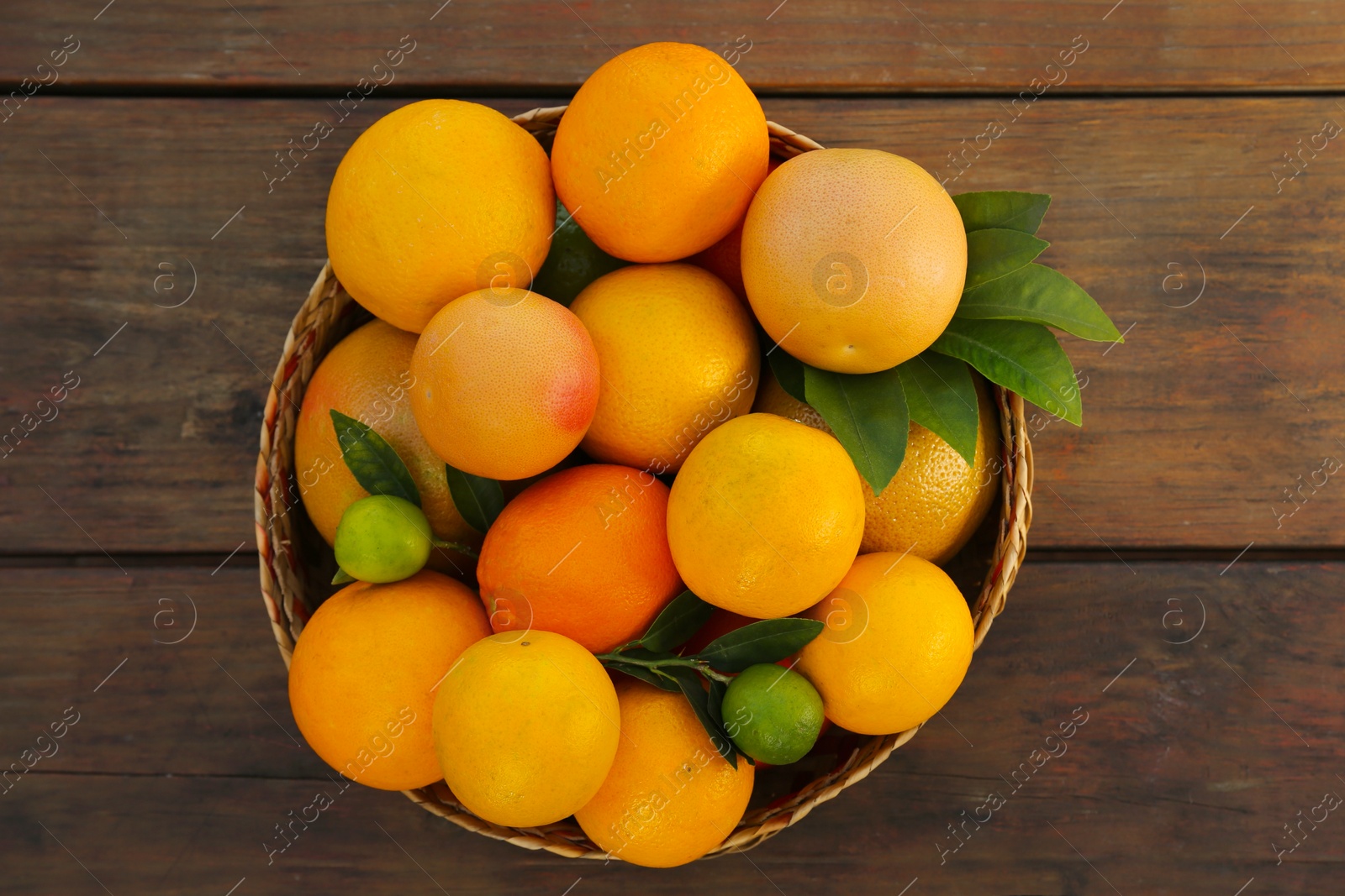 Photo of Wicker basket with different citrus fruits and leaves on wooden table, top view