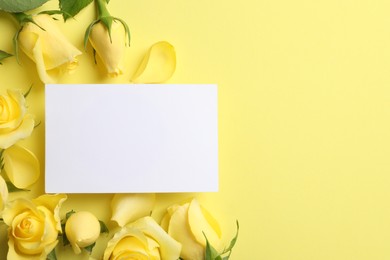 Beautiful roses, petals and blank card on yellow background, flat lay. Space for text