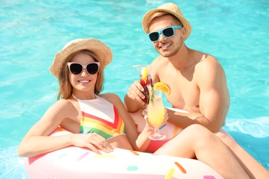 Young couple with cocktails in pool on sunny day