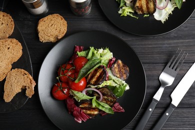 Photo of Delicious salad with roasted eggplant and basil served on black wooden table, flat lay