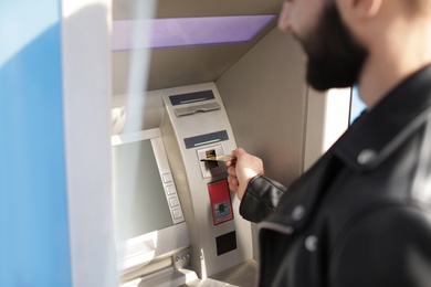 Photo of Man inserting credit card into cash machine outdoors, closeup