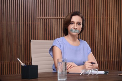 Image of Mature woman with taped mouth in office. Speech censorship