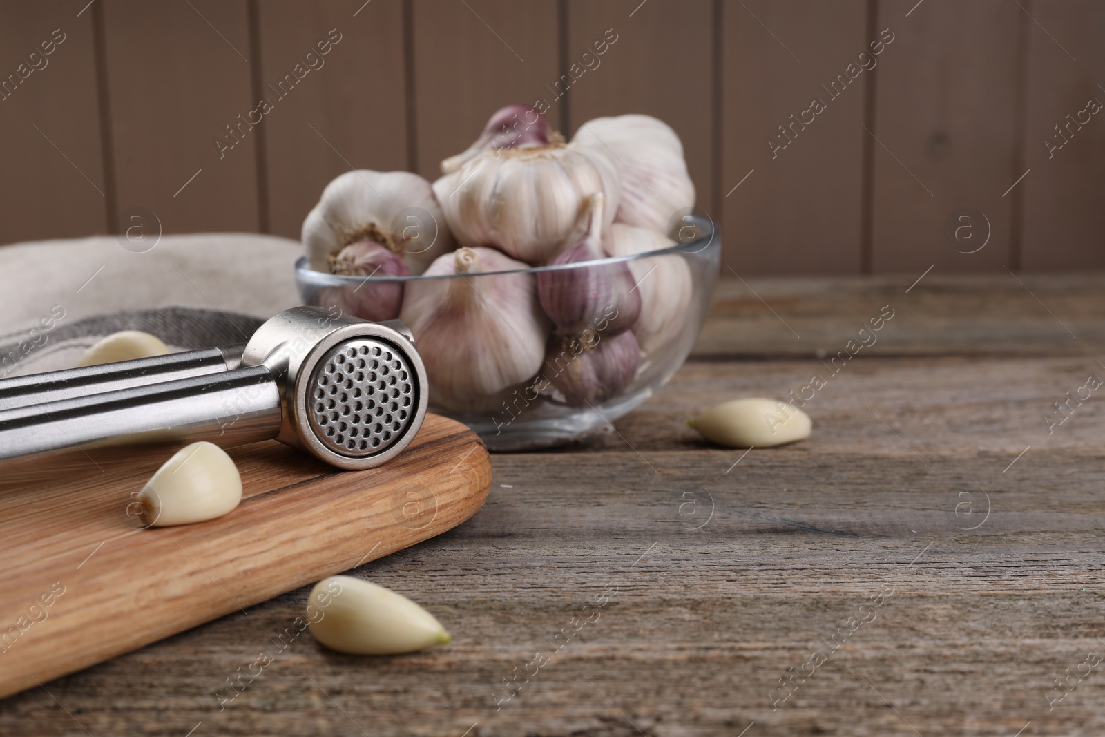 Photo of Garlic press and cloves on wooden table. Space for text