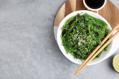 Photo of Tasty seaweed salad in bowl served on gray table, flat lay. Space for text