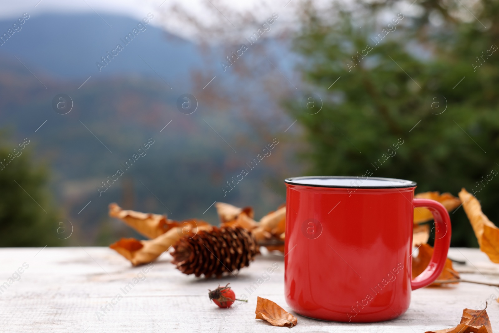 Photo of Mug of hot drink and autumn leaves on wooden table outdoors. Space for text