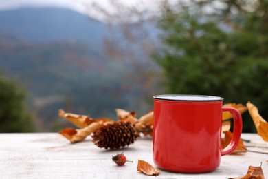 Mug of hot drink and autumn leaves on wooden table outdoors. Space for text