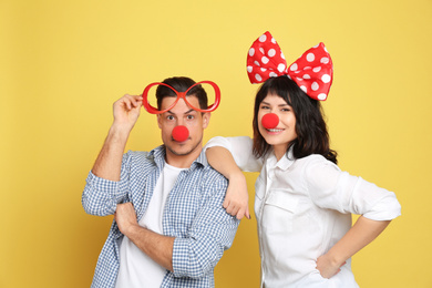 Photo of Couple with funny accessories on yellow background. April fool's day