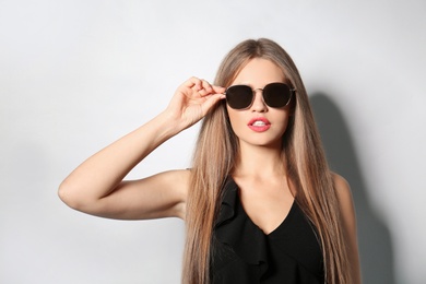 Photo of Young woman wearing stylish sunglasses on light background