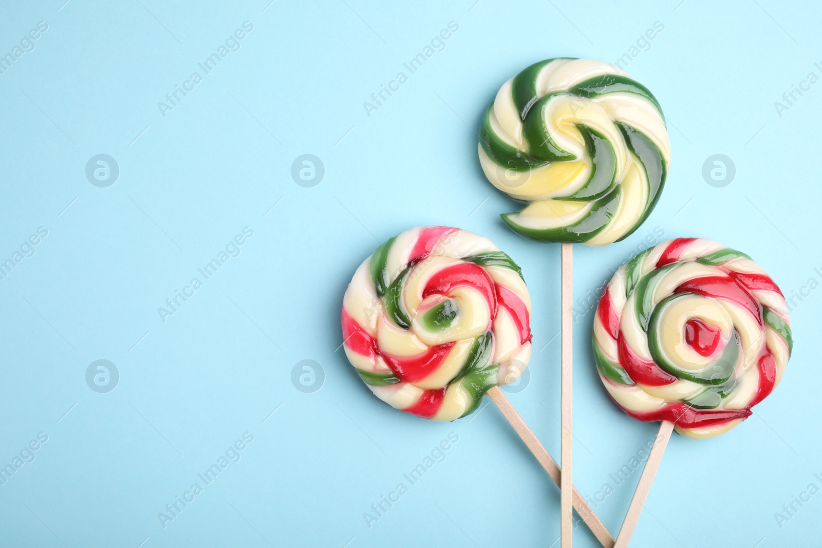 Photo of Colorful lollipops on light blue background, flat lay. Space for text