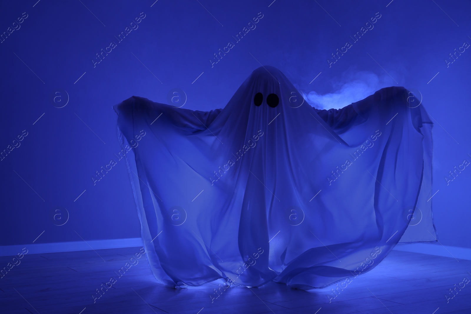 Photo of Creepy ghost. Woman covered with sheet in blue light