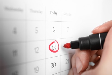 Photo of Woman marking Friday 13th on calendar, closeup. Bad luck superstition