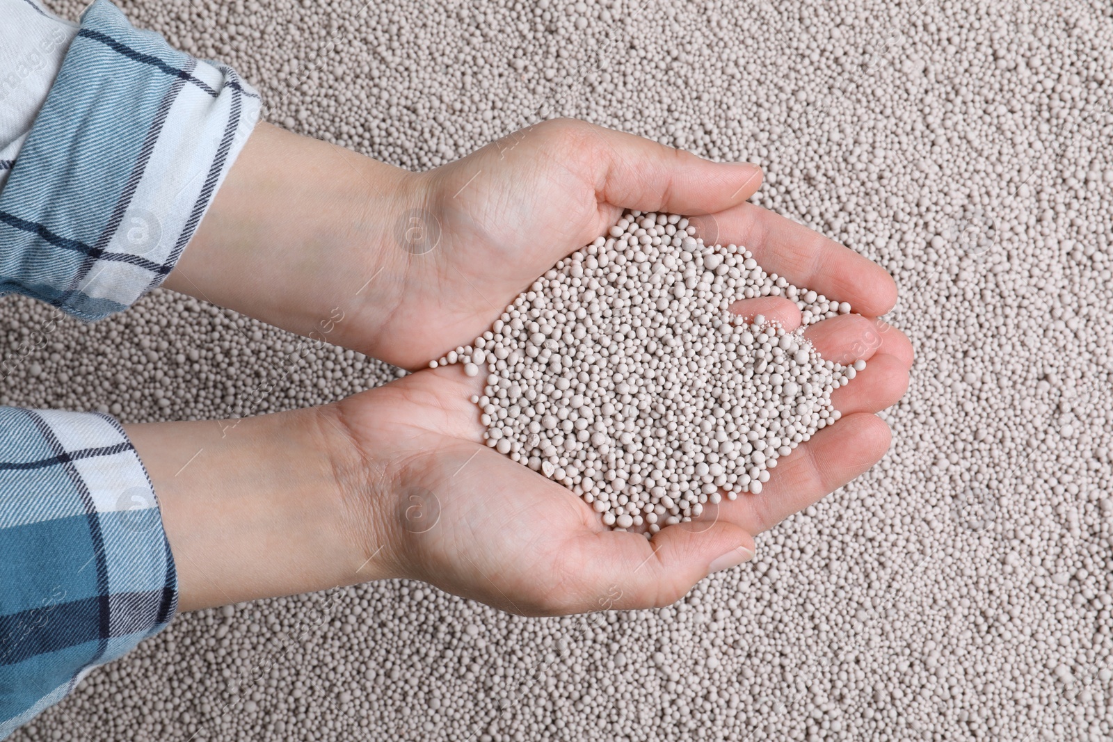 Photo of Woman holding chemical fertilizer over pellets, closeup. Gardening season