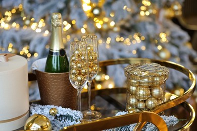 Photo of Glasses, baubles, bottle of sparkling wine and other Christmas decor on table against blurred background, closeup