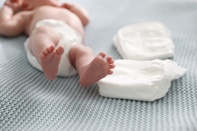 Photo of Cute little baby in diaper lying on bed, closeup