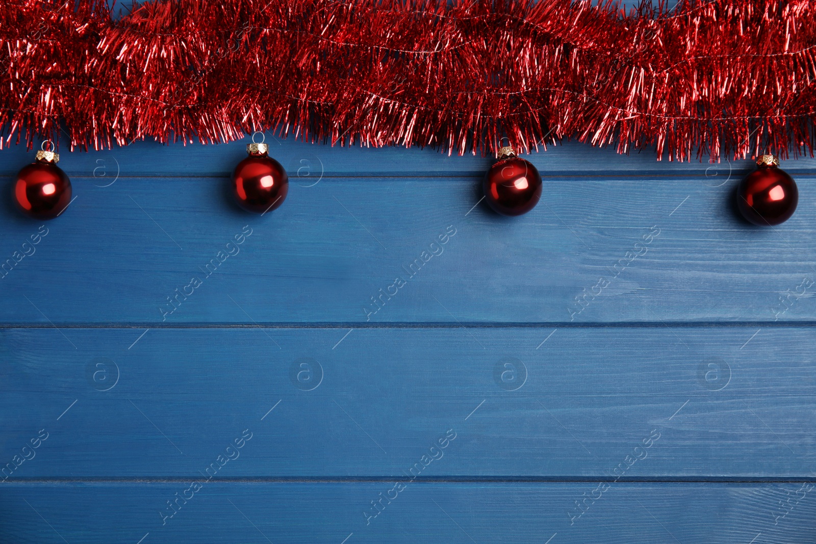 Photo of Red tinsel and Christmas balls on blue wooden background, flat lay. Space for text