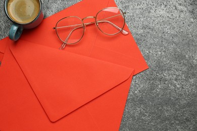 Photo of Red envelopes, cup of coffee and glasses on grey table, flat lay. Space for text