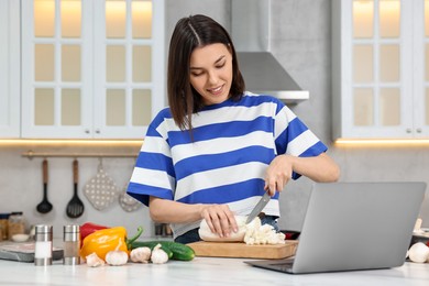Young woman cooking while watching online course via laptop in kitchen