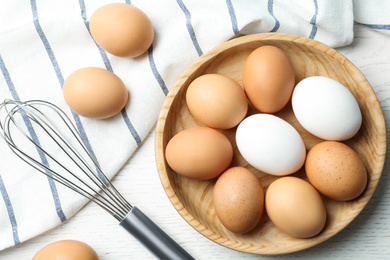 Photo of Chicken eggs and whisk on white wooden table, flat lay