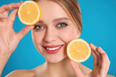 Photo of Young woman with cut lemon on blue background. Vitamin rich food