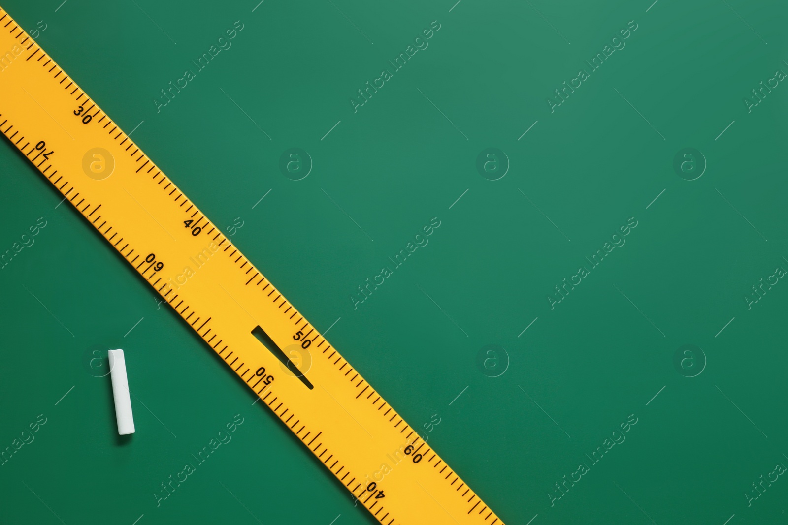 Photo of Ruler and chalk on green chalkboard, flat lay. Space for text