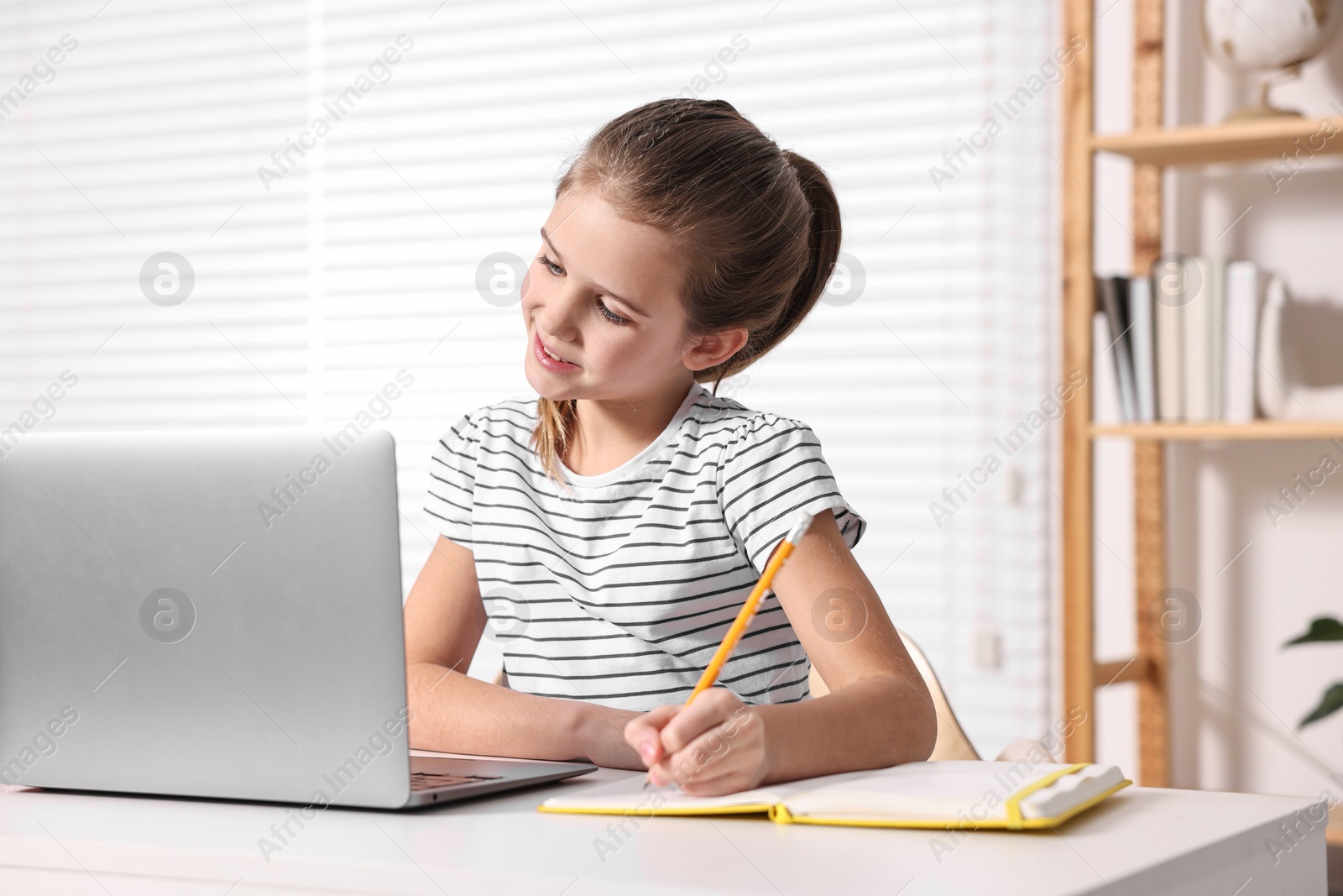 Photo of E-learning. Cute girl taking notes during online lesson at table indoors