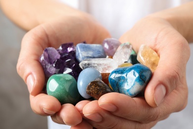 Young woman holding many beautiful gemstones on beige background, closeup