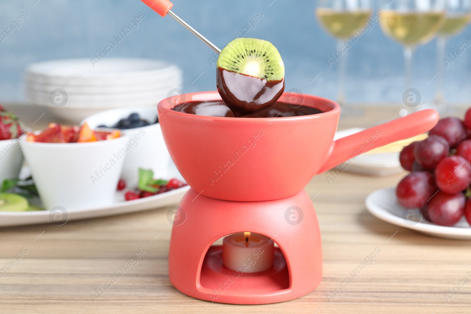 Photo of Dipping kiwi slice into pot with chocolate fondue on table