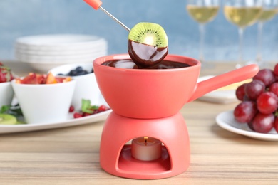 Photo of Dipping kiwi slice into pot with chocolate fondue on table