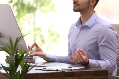 Photo of Young businessman meditating at workplace, closeup. Zen concept