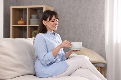 Photo of Beautiful young housewife with cup of drink on sofa at home