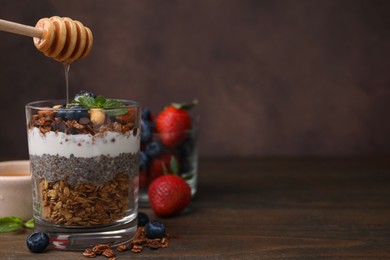 Photo of Pouring honey onto tasty granola with berries, yogurt and chia seeds at wooden table. Space for text