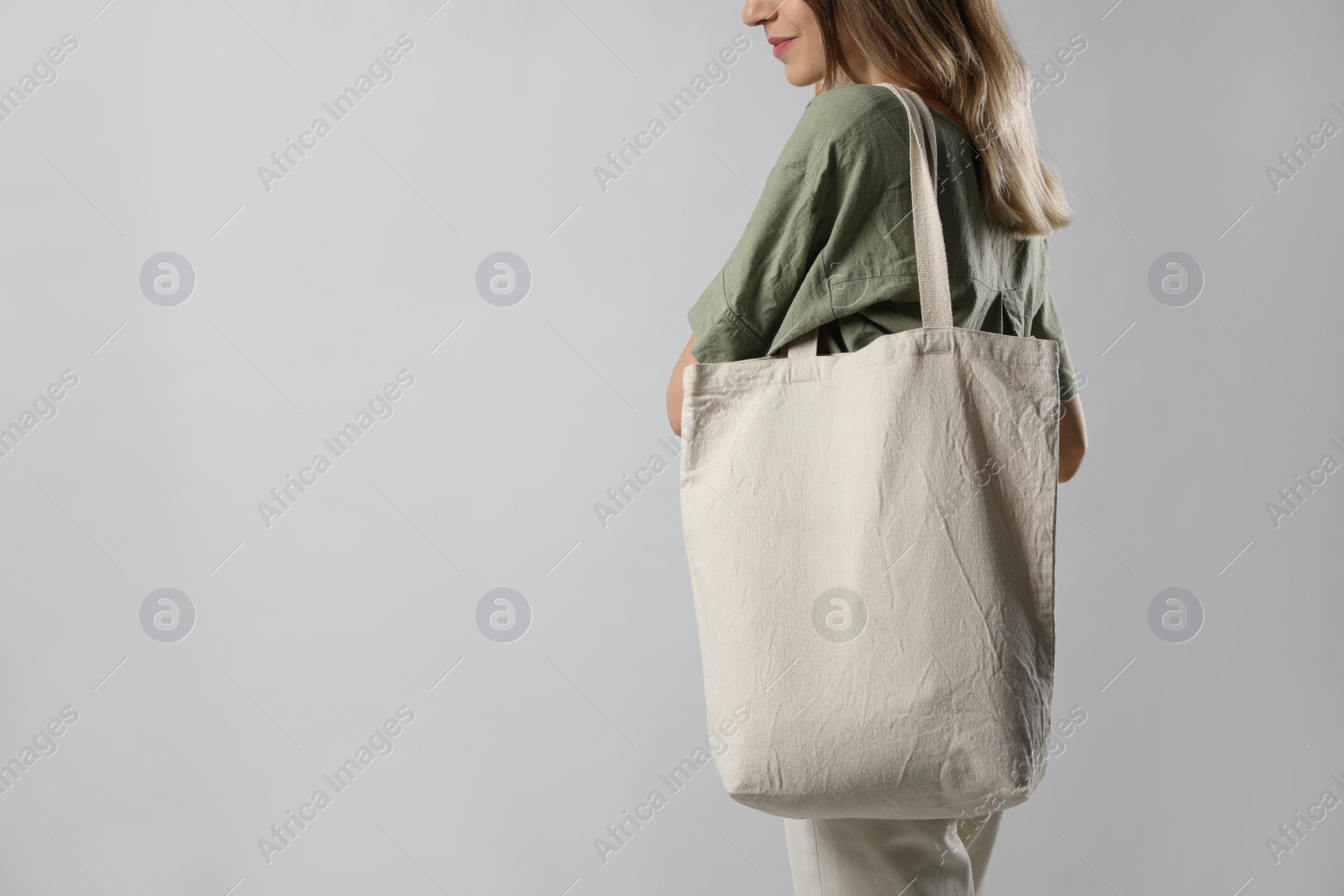 Photo of Young woman with blank eco friendly bag on light background, closeup. Space for text