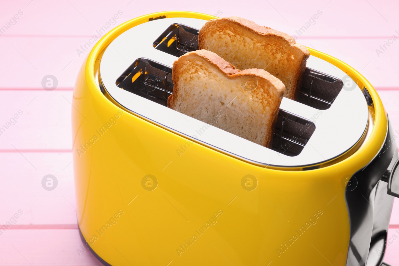 Photo of Yellow toaster with roasted bread on pink wooden table, closeup