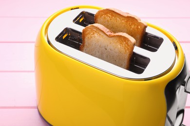 Photo of Yellow toaster with roasted bread on pink wooden table, closeup