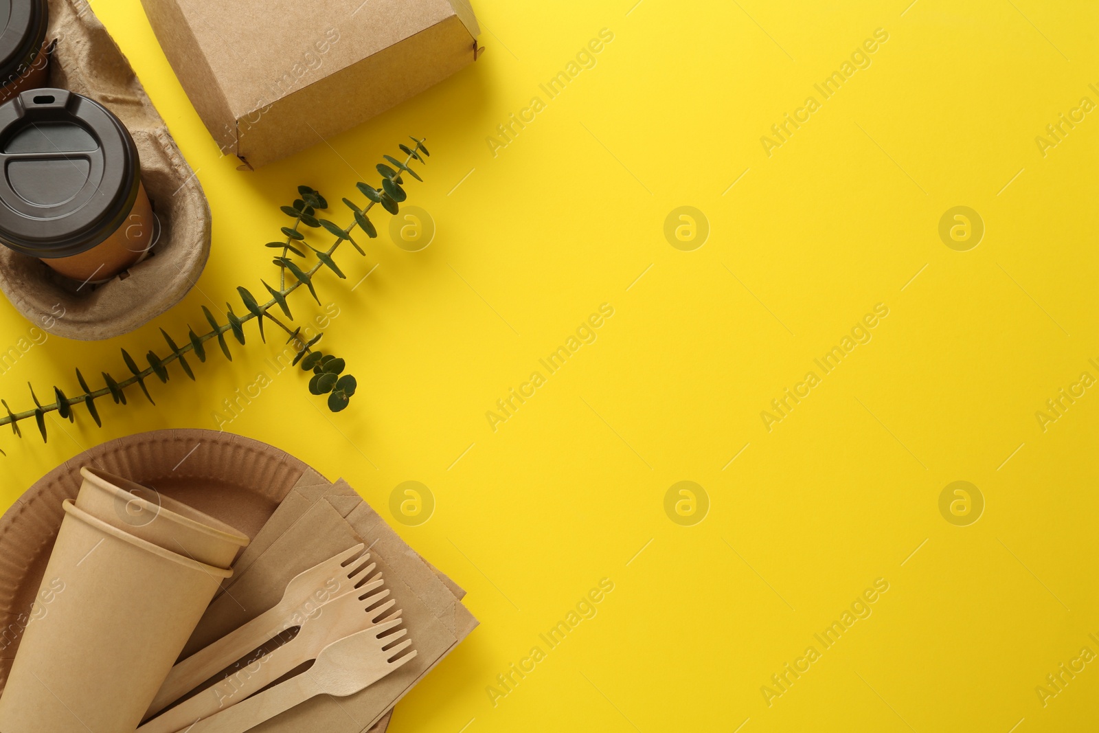 Photo of Flat lay of paper and wooden tableware with green twig on yellow background, space for text. Eco friendly lifestyle