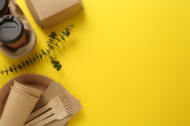 Photo of Flat lay of paper and wooden tableware with green twig on yellow background, space for text. Eco friendly lifestyle