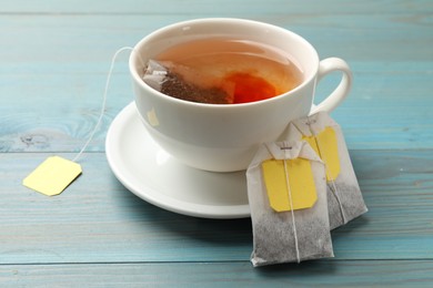 Tea bags and cup of aromatic drink on light blue wooden table, closeup