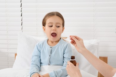 Mother giving cough syrup to her daughter in bedroom
