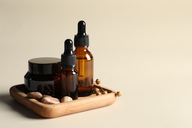 Photo of Wooden tray with bottles of cosmetic serum, jar and stones on beige background. Space for text