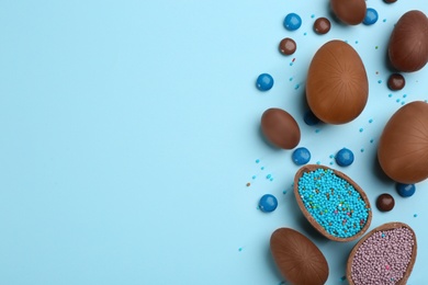 Photo of Sweet chocolate eggs and candies on light blue background, flat lay. Space for text