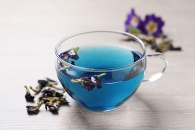 Glass cup of organic blue Anchan on white wooden table. Herbal tea